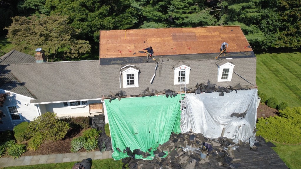 Before — roof tear-off in progress on a white Fairfield County home with plywood deck exposed