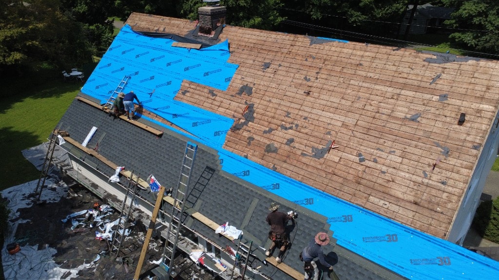 Before — aerial view of asphalt shingle roof replacement in progress with tear-off, underlayment, and crew on a Fairfield County home