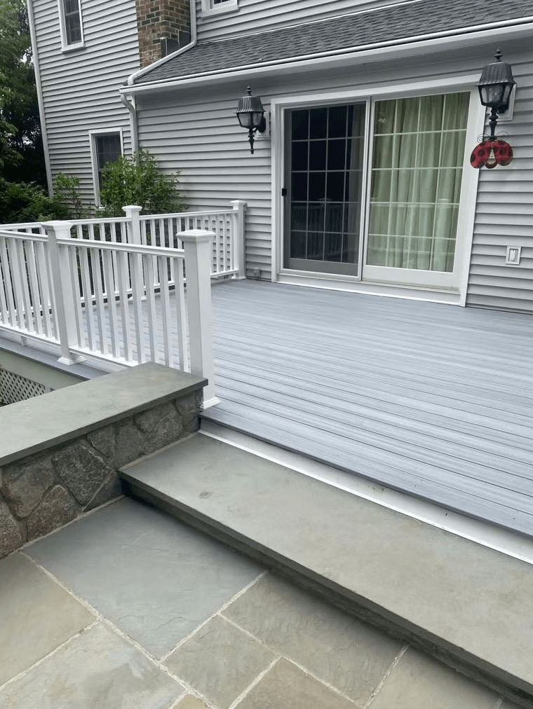 Custom grey composite deck with white railings and flagstone patio transition in Fairfield County, CT